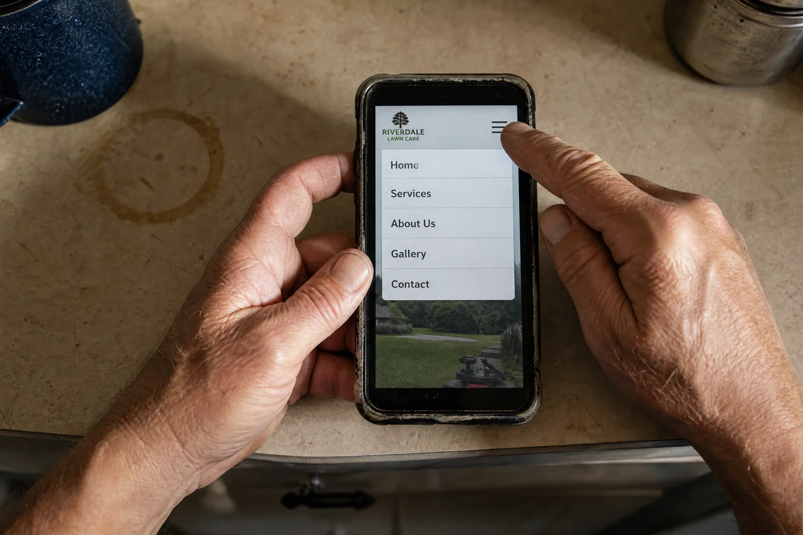 Hands holding phone displaying Riverdale Lawn Care website with menu open